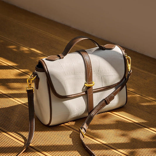 Elegant white handbag with brown leather straps and gold accents on a wooden surface